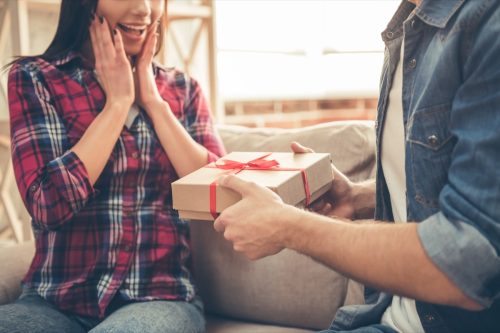 Woman reacting happily to man handing her a wrapped gift