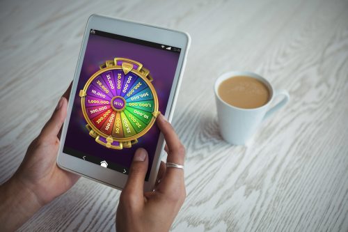 Multi colored fortune of wheel on mobile display against cropped hands of woman holding tablet at table