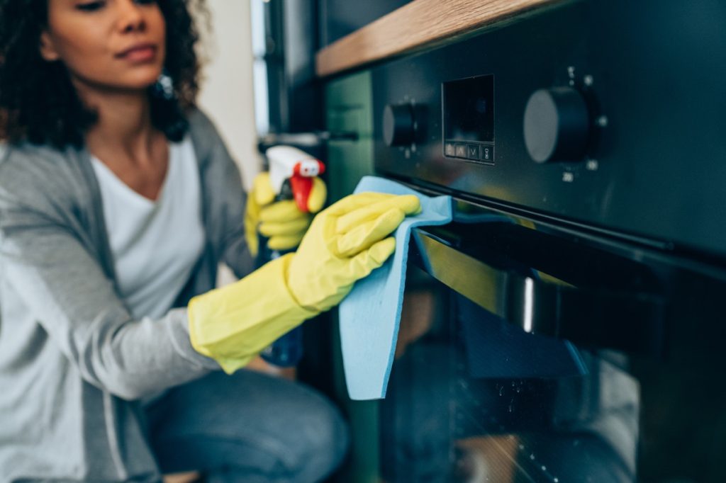 Woman using spray bottle and rag to clean the outside of her oven