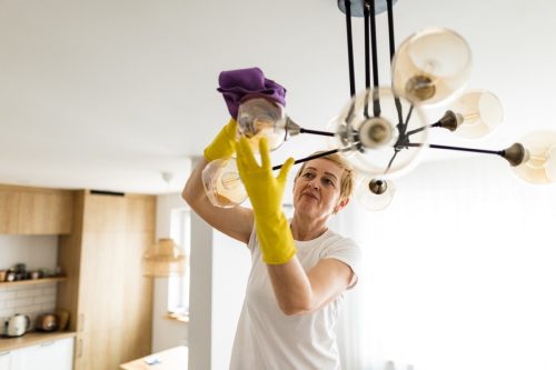 woman thoroughly wipes the shade in the lamp with a rag at home