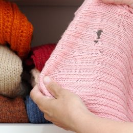 Cropped woman hands holding pink sweater with hole made by moth