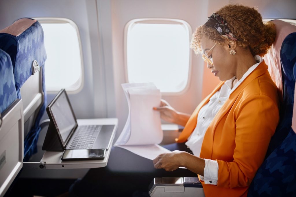 Woman sitting in an airplane seat and using a laptop.