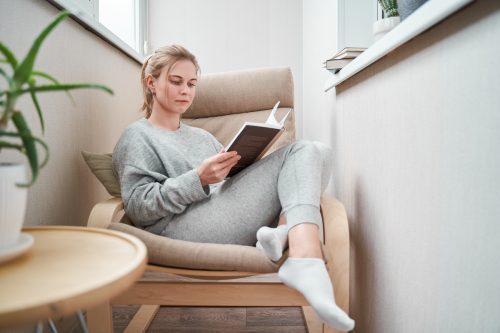 Young girl reading book while sitting on beige armchair in a cozy reading nook