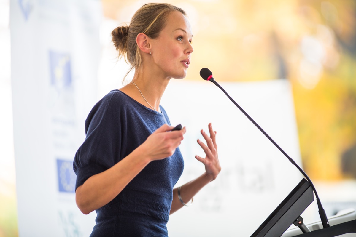 Woman in a navy blue dress Giving a Speech at a podium