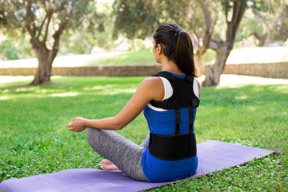 A beautiful girl in a park dressed in sportswear wearing Back posture corrector sit on yoga mat in ypoga pose. Different views. Lifestyle, outdoor.