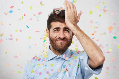 man looking regretful while wearing a party hat covered in confetti