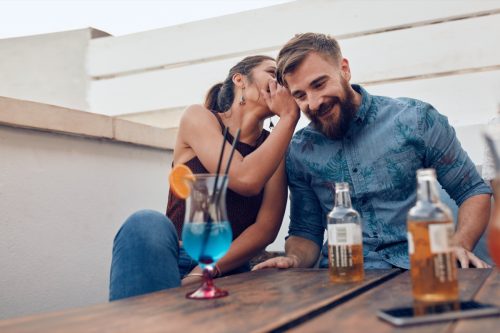woman whispering funny rizz lines to man at a bar
