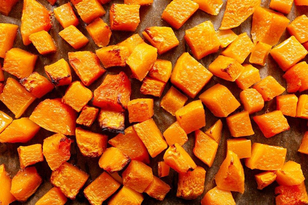 A top view of diced butternut squash cooking on a baking sheet.