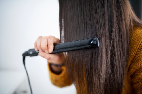 Close up of a brunette woman using a hair straightener.