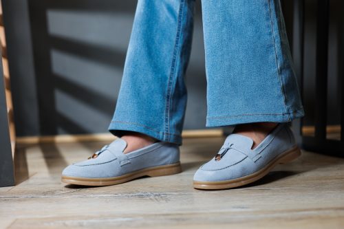 Slender female legs in jeans and blue loafers.