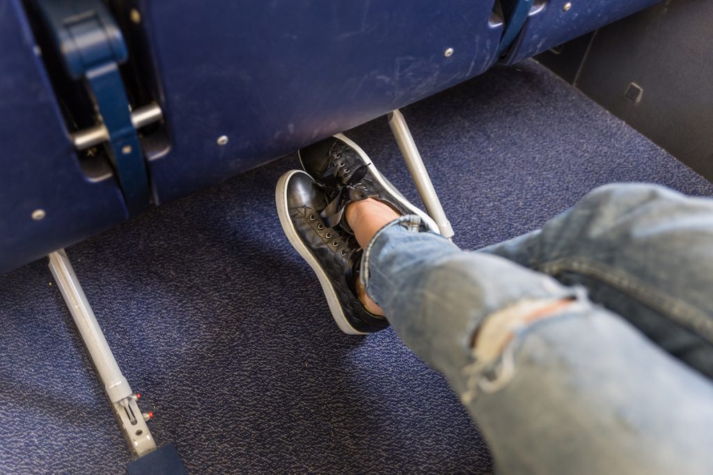 Woman sitting in an airplane seat stretching her legs, wearing ripped jeans and black sneakers