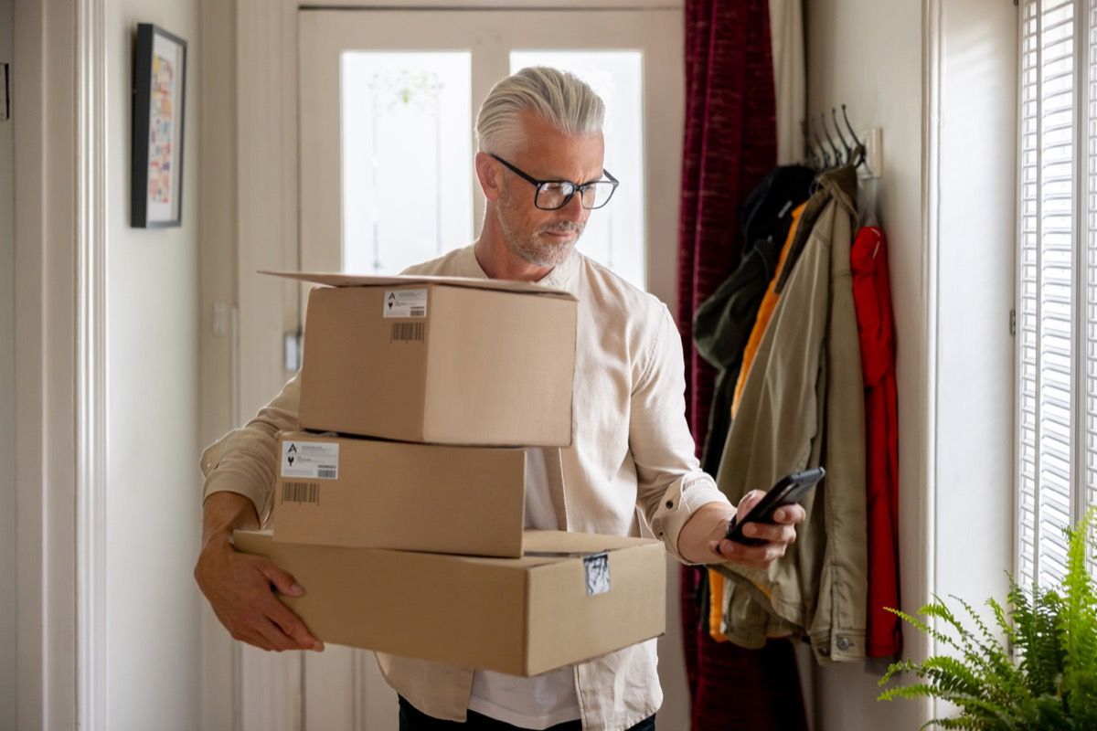 Man receiving a package at home and getting a notification on his cell phone