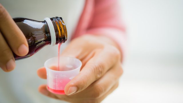 Closeup woman pouring medication or antipyretic syrup from bottle to cup. Healthcare, people and medicine concept -