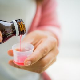 Closeup woman pouring medication or antipyretic syrup from bottle to cup. Healthcare, people and medicine concept -