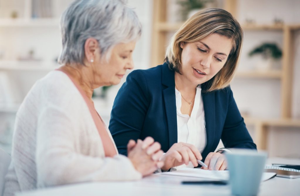 Young woman helping senior woman with paperwork at desk