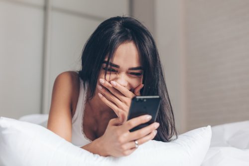 woman in bed laughing while reading her text messages
