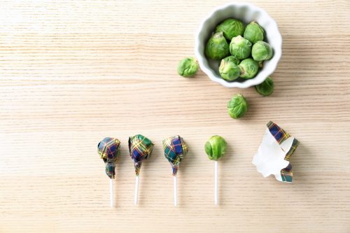Brussel sprouts with lollipop sticks in candy wrappers on table.