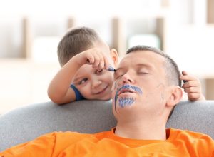 little boy drawing on his father's face as he sleeps