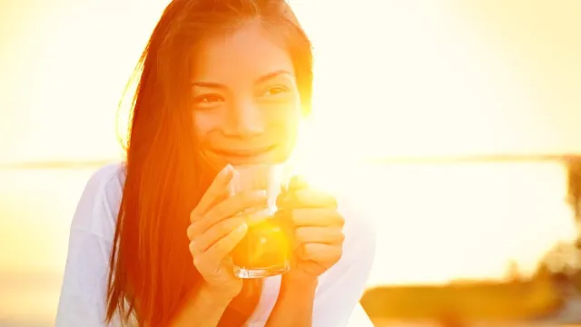 smiling woman drinking coffee in the sunlight