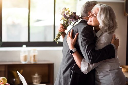 Woman holding flowers hugging man, celebrating wedding anniversary