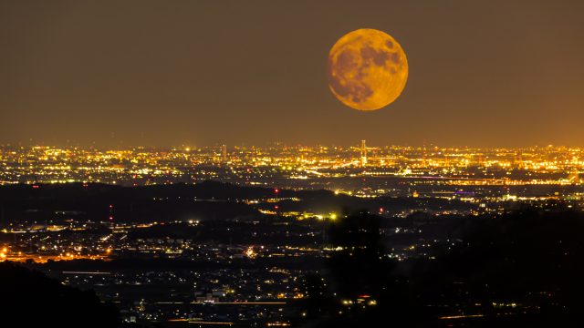 An orange Harvest Full Moon rising over a city at night