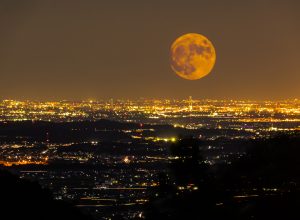 An orange Harvest Full Moon rising over a city at night