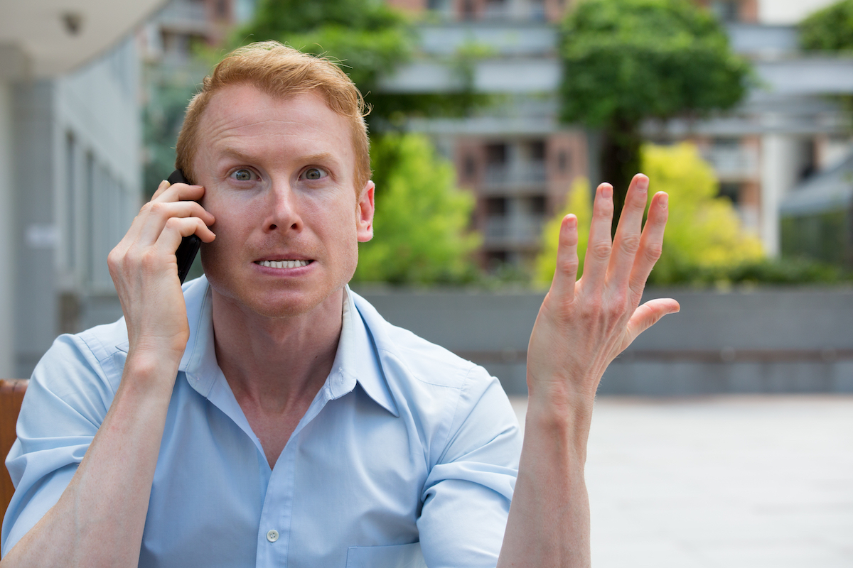 A man sitting outside on the phone looking very irritated and annoyed.