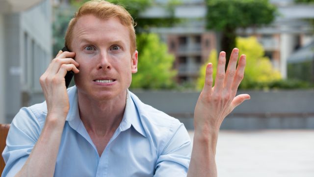 A man sitting outside on the phone looking very irritated and annoyed.