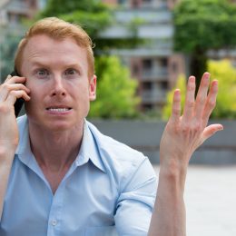 A man sitting outside on the phone looking very irritated and annoyed.