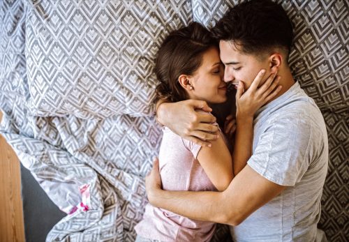 Man and woman lying on bed at home and cuddling, embracing and enjoying weekend together