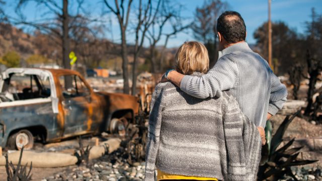 A couple hugging while looking at the effects of a natural disaster, likely a fire