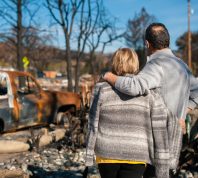 A couple hugging while looking at the effects of a natural disaster, likely a fire