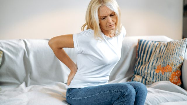 A mature woman sitting on her couch holding her lower back in pain