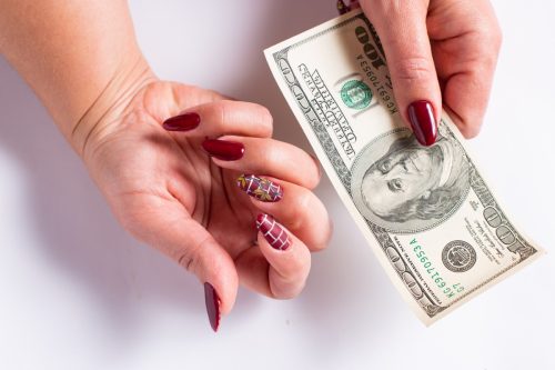 Female hands with manicure holding 100 dollars and showing new pattern manicure, on a white background.