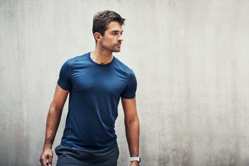 Shot of a sporty young man standing against a grey wall while exercising outdoors