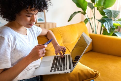 Close up of woman sitting on the couch using credit card and laptop to shop online from home. 