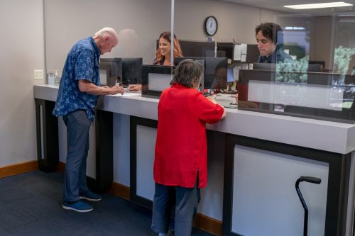 Two customer service representatives assist happy senior adult customers while working at the reception desk of a medical office or bank.