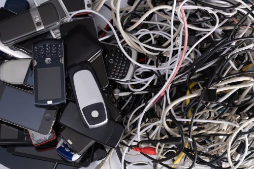 Pile of tangled old smart technology wires, charging cables and used obsolete mobile phones. 