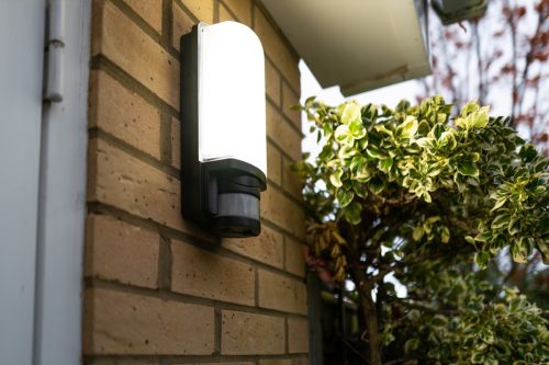 Exterior PIR LED security light seen glowing following body motion detection via its Infra Red sensor. Located by a garage door