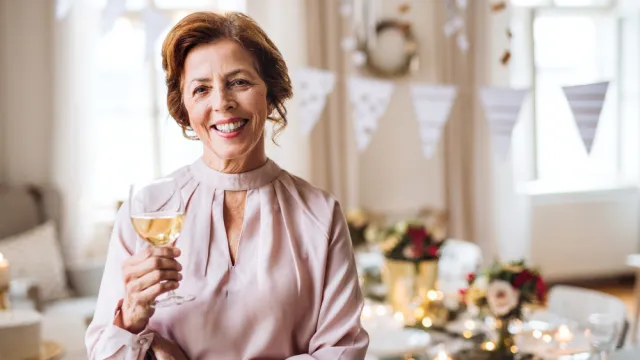 Portrait of smiling senior woman in pink blouse hosting a party with wine or champagne