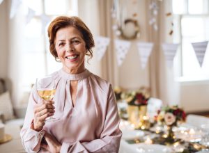 Portrait of smiling senior woman in pink blouse hosting a party with wine or champagne