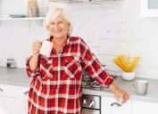 Happy smiling senior woman in kitchen at home with plaid flannel shirt and coffee mug