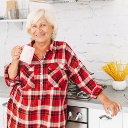Happy smiling senior woman in kitchen at home with plaid flannel shirt and coffee mug