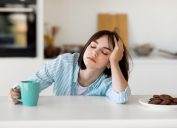 Sleepy young woman drinking coffee at kitchen counter
