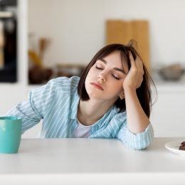 Sleepy young woman drinking coffee at kitchen counter