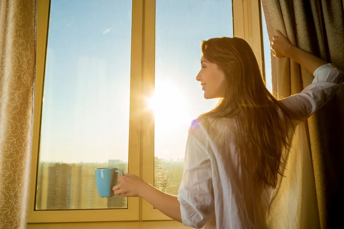 Яркое солнце светит в окна домов. Девушка у окна. Она девушка. Солнечное утро в окне. Женщина возле окна.