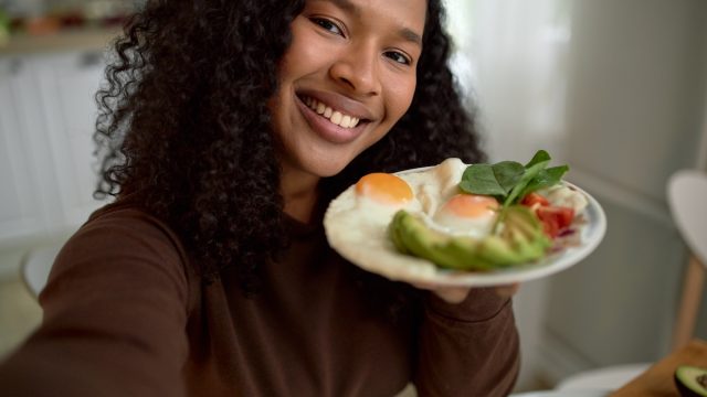 Smiling young woman with plate of eggs avocados