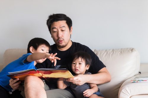 Young boy points to story book dad is reading aloud