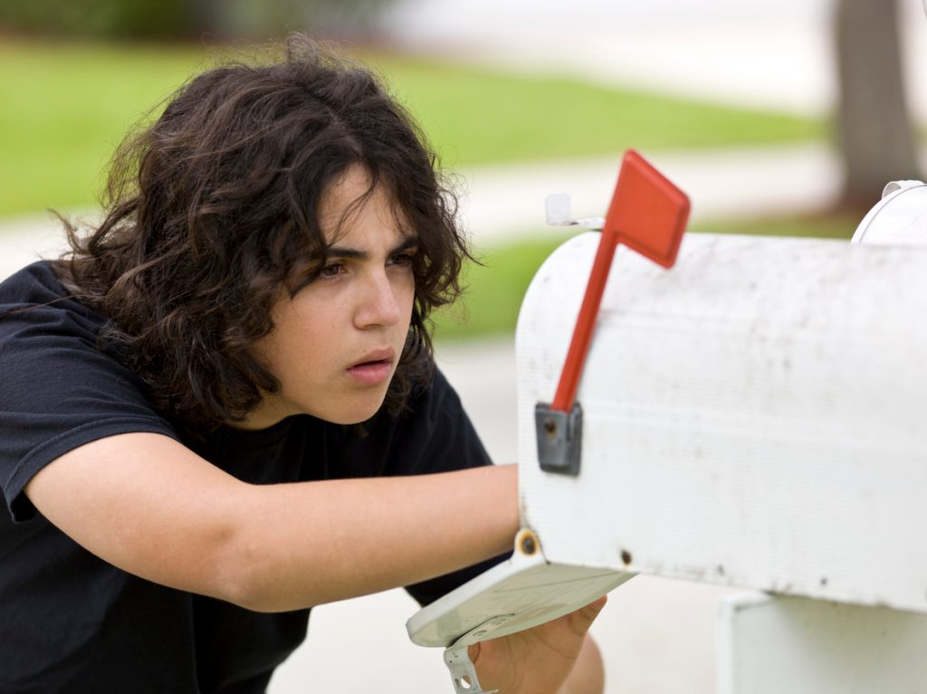 A young person looking into a white mailbox