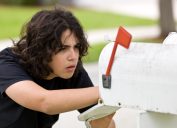 A young person looking into a white mailbox potentially stealing letters or packages